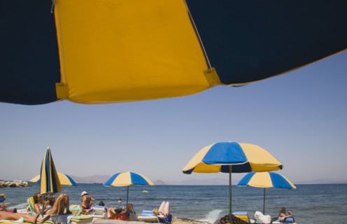Kos, Dodecanese Islands, Greece. People sunbathing on loungers some beneath yellow and blue striped