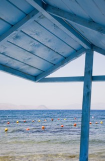 Kos, Dodecanese, Greece. View over red and yellow floats in water part framed by roof of blue