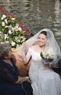 Venice, Veneto, Italy. Smiling bride in wedding dress and veil carrying bouquet seated beside