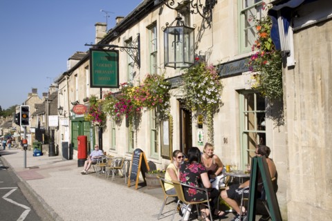 Burford, Gloucestershire, England. Tourists sat outside the Golden Pheasant Hotel in the Cotswolds.