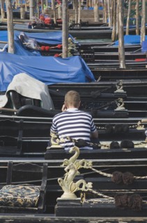 Venice, Veneto, Italy. Gondolier in striped shirt using mobile phone while sitting in one of a line