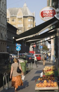 Budapest, Pest County, Hungary. Woman walking past local grocer and fruit display under black