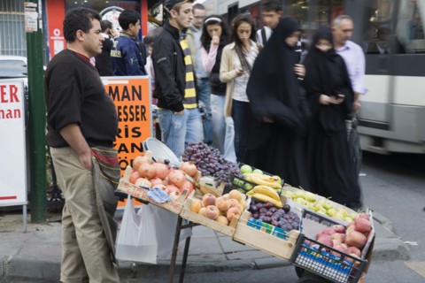 Istanbul, Turkey. Sultanahmet. Two women wearing burqa and veil passing fresh fruit stall with male