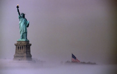 Liberty Island, New York, USA. Statue of Liberty and Stars and Stripes Flag on misty morning. USA