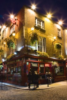 Ireland, County Dublin, Dublin City, Temple Bar Pub illuminated at night with people walking past