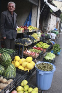Albania, Tirane, Tirana, Grocer beside his shop front display of fruit and vegetables including