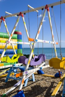 England, West Sussex, Bognor Regis, Colourful amusement swings on the pebble shingle beach by the