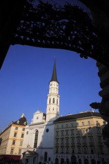 Angled view St Michaels Church exterior facade and spire against blue sky framed by decorative