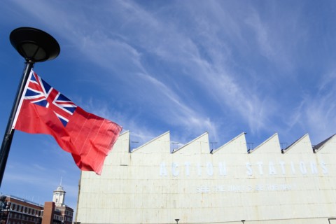 Historic Naval Dockyard Red Ensign merchant marine flag flying from flagpole with Action Stations