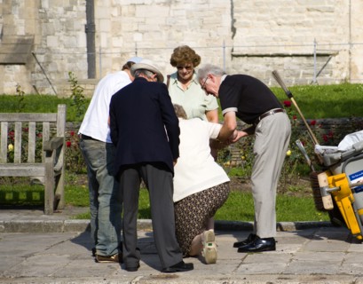 People helping an elderly lady to stand up after she has fallen on the pavement sidewalk outside
