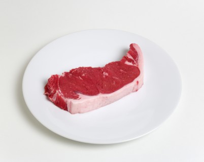 Slice of raw uncooked sirloin steak on a round white plate against a white background. Photo: Paul