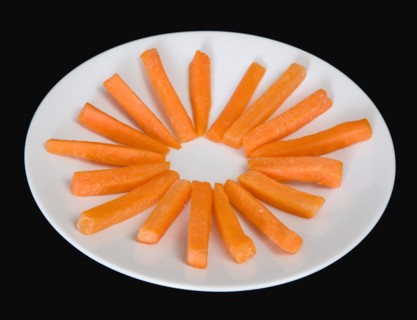 Slices of raw uncooked carrot on a white plate against a black background. Photo: Paul Seheult