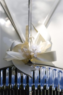 Cream ribbon tied in bow on bonnet of vintage white Daimler wedding car. Photo: Paul Seheult