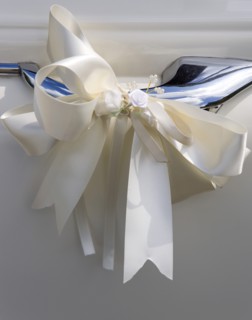 Cream ribbon tied in bow on door handle of vintage white Daimler wedding car. Photo : Paul Seheult