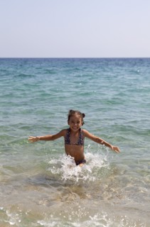 Young smilling girl playing at the sea throwing water and laughing. Photo : Athanasios Papadopoulos