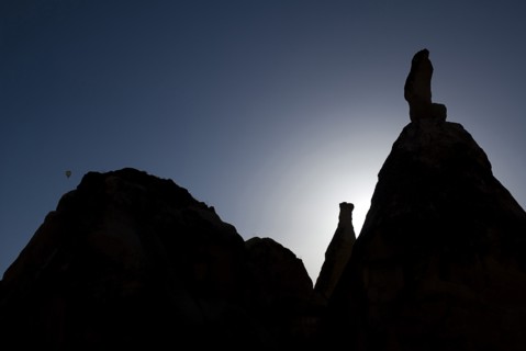 Distant hot air balloon in flight over silhouetted landscape of eroded rock forms. Photo: Hugh