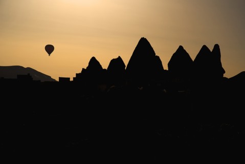 Distant hot air balloon in flight over silhouetted landscape of eroded rock forms. Photo: Hugh