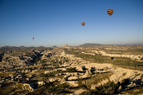 Hot air balloons in flight over landscape in early morning sunlight with Uchisar town in background