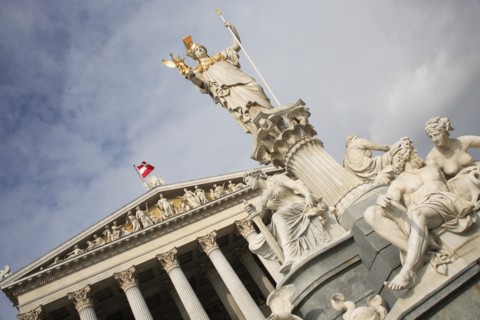 Angled view of statue of Athena raised on pillar above fountain in front of the Parliament building