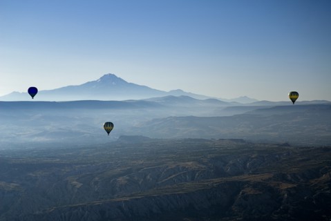 Early morning with hot air balloons in flight mist drifting across landscape and Mount Erciyes in