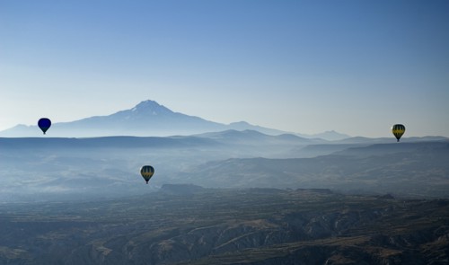 Early morning with hot air balloons in flight mist drifting across landscape and Mount Erciyes in