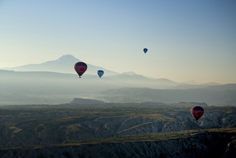 Early morning with hot air balloons in flight above tufa landscape with Mount Erciyes in the