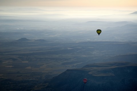 Hot air balloons in flight over landscape in misty early morning light with pale orange sky. Photo: