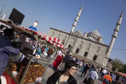 Turkey, Istanbul, Eminonu Yeni Camii New Mosque with pretzel vendor in the square. 
Photo :