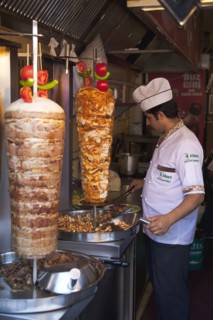 Turkey, Istanbul, Sultanahmet man in kebab restaurant carving shawarma from skewered meats. 
Photo