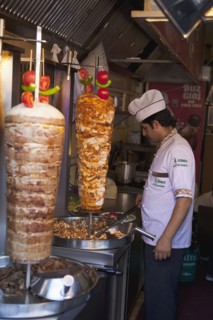 Turkey, Istanbul, Sultanahmet man in kebab restaurant carving shawarma from skewered meats. 
Photo