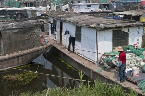 China, Jiangsu, Qidong, Man in a red shirt and straw hat fishing with a rod and line off his boat