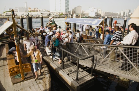 Tourists board Abra water taxi moored on the Creek with Bur Dubai heritage skyline behind.