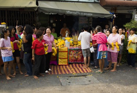 Women in front of Guanyin female Goddess of Mercy statue with offerings for parade celebrating local temple.