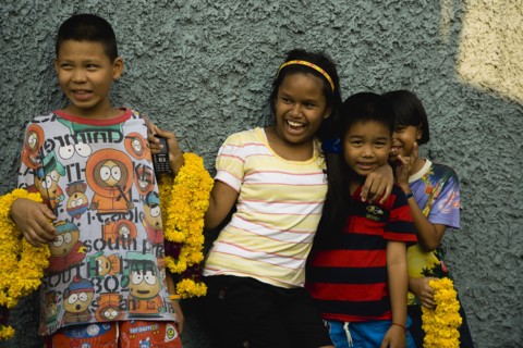 Thai children with mobile phone and floral garlands to celebrate the annual blessing of local temple .