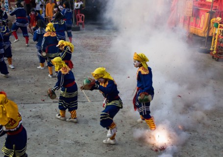 Thai boys in Chinese character costume dancing and drumming with firecrackers exploding at local temple.