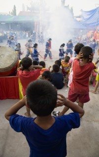 Thai boys cover their ears watching performance with firecrackers exploding at local temple.