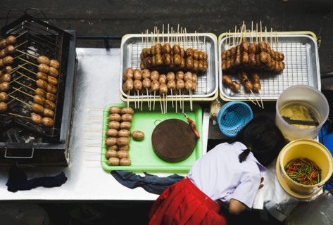 Primary School girl in uniform at sausage stall outside BTS Skytrain station.