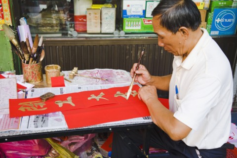 Calligrapher painting Gold characters on red paper auspicious colours for Chinese New Year.