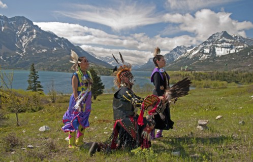 Blackfoot Indians dressed for a Pow Wow with Middle and Upper Waterton Lakes the Rocky Mountains and the Prince of Wales Hotel in the background. The park is a UNESCO World Heritage Site Blue sky with...