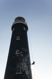 Man cleaning Lighthouse tower with pressure washer whilst abseiling.
