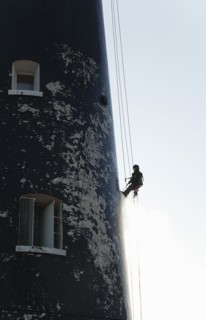 Man cleaning Lighthouse tower with pressure washer whilst abseiling.
