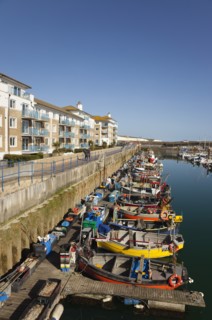 View over fishing boats moored in the Marina with apartment buildings behind.