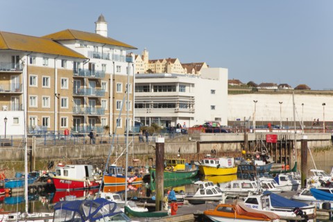View over fishing boats moored in the Marina with apartment buildings behind.
