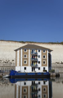 Apartment building in marina with moored barge and chalk cliffs behind.