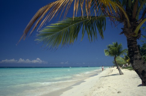 West Indies, Jamaica, Negril, Sandy stretch of beach beside flat aquamarine water with woman