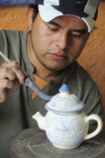 Mexico, Puebla, Talavera ceramic artist at Armando Gallery applying blue detail to raised design on