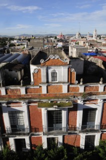 Mexico, Puebla, View across city rooftops with red brick and white facade of building in foreground