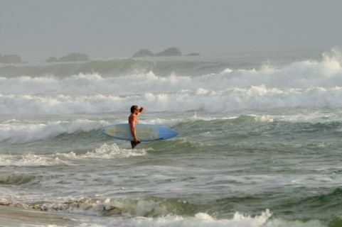 Mexico, Oaxaca, Puerto Escondido, Surfer walking through surf carrying board. Photo : Nick Bonetti