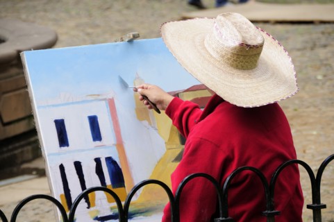 Mexico, Michoacan, Patzcuaro, Painter in Plaza Vasco de Quiroga applying paint to canvas using
