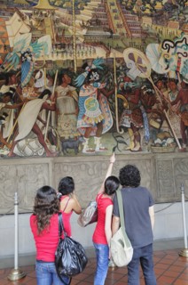 Mexico, Federal District, Mexico City, Group of visitors looking at mural by Diego Rivera depicting